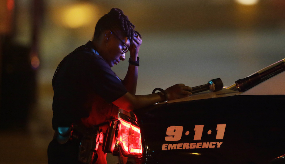 A Dallas police officer, who did not which to be identified, takes a moment as she guards an intersection in the early morning after a shooting in downtown Dallas, Friday, July 8, 2016. At least two snipers opened fire on police officers during protests in Dallas on Thursday night; some of the officers were killed, police said. (AP Photo/LM Otero)