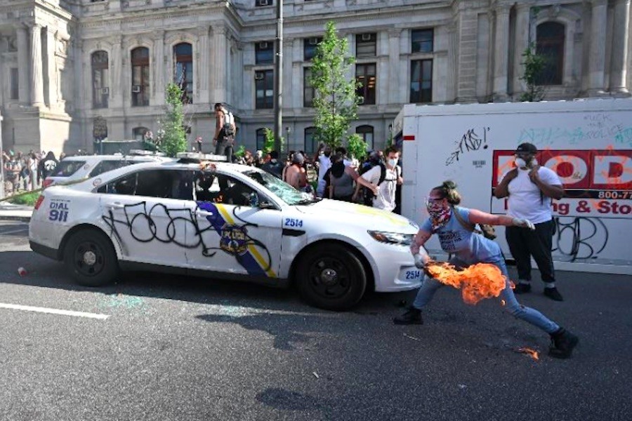 the FBI says this photo shows Lore Blumenthal lighting a Philadelphia police car on fire during a George Floyd protest