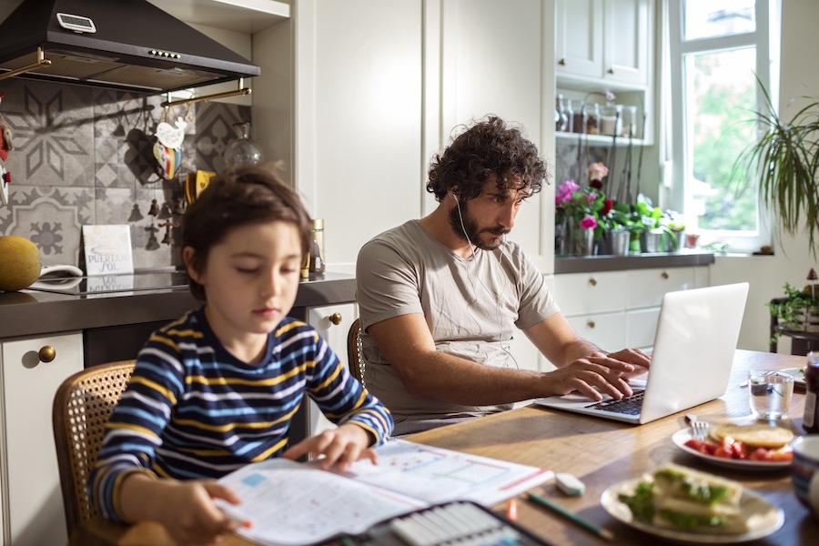 A child participating in virtual school while his father attempts to work from home as well.