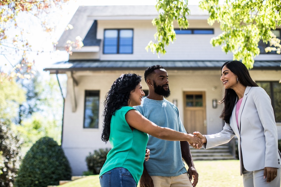 couple meeting a real estate agent in front of a house